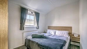 Une chambre à coucher avec un lit, une table de chevet, une fenêtre avec des rideaux et un radiateur.