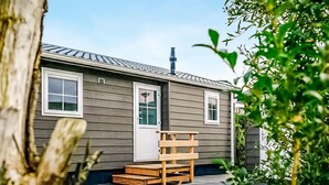 Une maison de plain-pied à l’extérieur gris, avec des encadrements de fenêtres et de portes blancs, une cheminée et un banc en bois à l’extérieur.