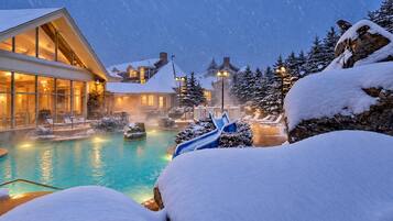 Un resort con piscina climatizada, sillas de descanso y árboles cubiertos de nieve.