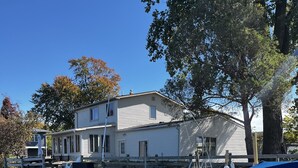 Ein Haus mit einem Steg, der sich in ruhiges Gewässer erstreckt, ein Boot namens 'RINKER' liegt an dem Steg festgemacht, und ein klarer, blauer Himmel.