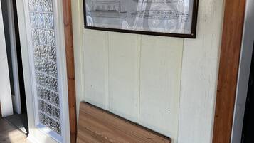 Een ingelijste blauwdruk van een scheepsinterieur, een decoratieve glazen deur en een houten bank.