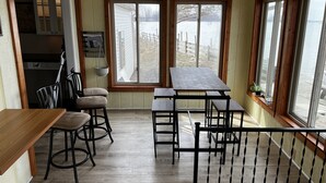 Ein gemütliches Zimmer mit Holzboden, einem Tisch, zwei Stühlen und Seeblick durch große Fenster.