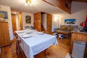 Un comedor con una mesa dispuesta para cuatro, armarios de madera, una escalera y un sofá al fondo.