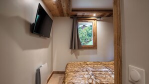 A bedroom with a bed, a TV mounted on the wall, a window with curtains, and a radiator. - Appartement ski in and out in the center of Méribel (Les Allues)