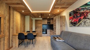 A modern interior with wooden walls, a dining area, a kitchen, and a grey sofa. - Appartement ski in and out in the center of Méribel (Les Allues)