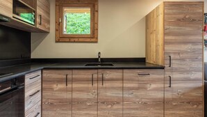 A modern kitchen with wooden cabinetry, a black countertop, and a window above the sink. - Appartement ski in and out in the center of Méribel (Les Allues)