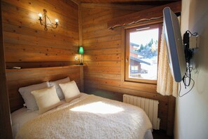 A cozy wooden cabin room with a bed, a window, and a wall-mounted heater. - Appartement on the slopes in Méribel Mottaret (Meribel Les Allues)