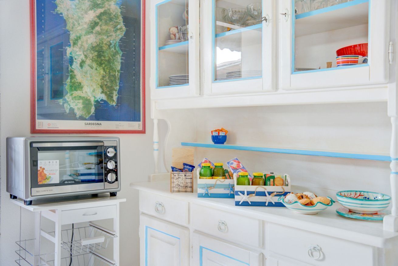 Een keuken met witte kasten, een magnetron en een kaart van Sardinië boven de kasten.