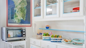 Une cuisine avec des meubles blancs, un four à micro-ondes et une carte de la Sardaigne accrochée au-dessus des meubles.