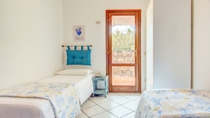 Une chambre avec deux lits, une petite table, une porte donnant sur un espace extérieur et une œuvre d’art accrochée au mur.