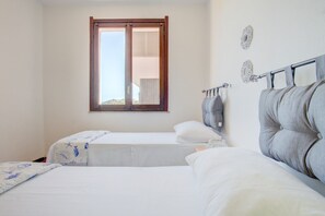 A bedroom with two beds, a window with blinds, and decorative wall mirrors. - Palau Port-Maddalena - APT - Home and More (Palau)