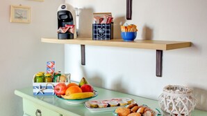 Een aanrecht met een koffiezetapparaat, een doos koffiecups, een broodmand, een fruitmand, een bord met koekjes en een decoratieve lantaarn.