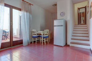 A small, bright room with a dining table and chairs, a refrigerator, and a staircase.