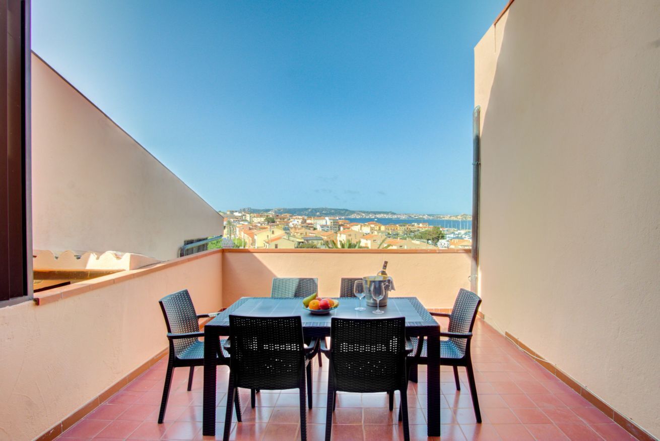 Ein Balkon mit Tisch, Stühlen, einer Flasche und einer Schüssel mit Obst.