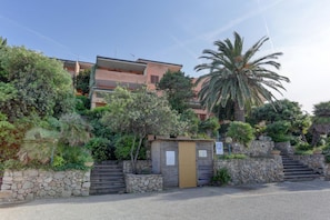 A multi-story building with a stone wall entrance, palm trees, and a clear sky. - Palau Port-Maddalena - APT - Home and More (Palau)