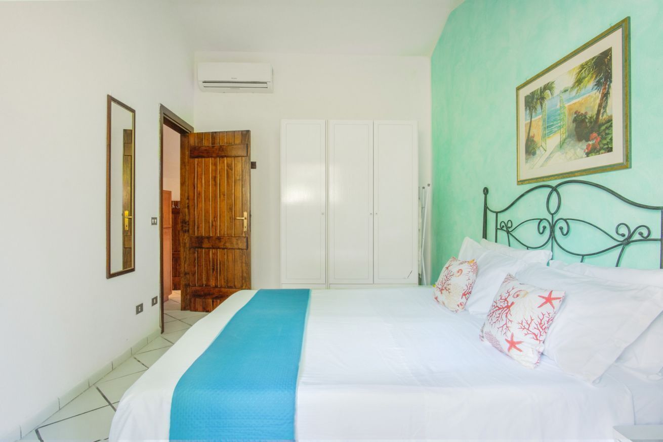 Un dormitorio con cama, puerta de madera, armarios blancos y un cuadro en la pared.