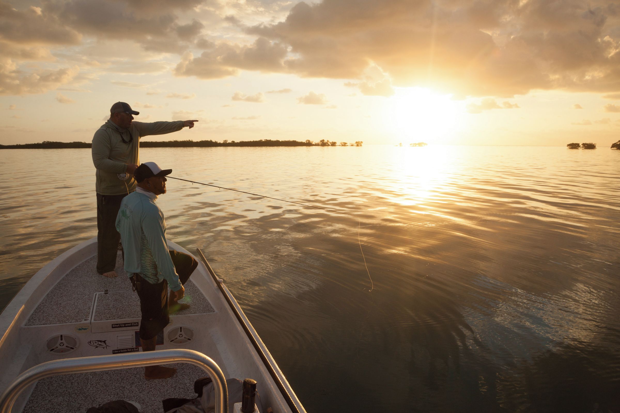 A boat with two people fishing, a clear sky, and a sunset.