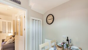 A dining area with a wooden table set for four, a clock on the wall, and a door leading to a bedroom. - Pennypot Cottage - UK41787 (Kettlewell)
