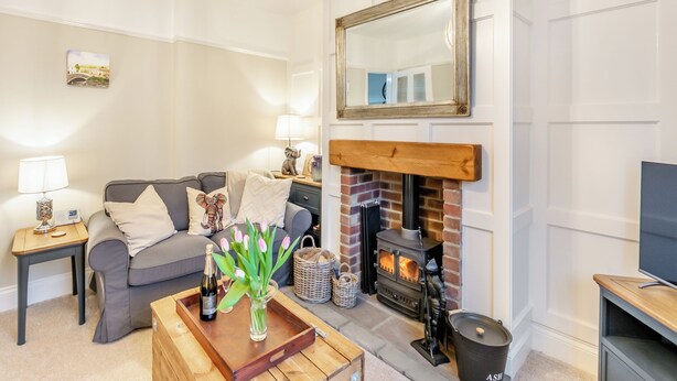 A living room with a fireplace, a sofa, a coffee table with a bottle and flowers, and a television on a stand. - Pennypot Cottage - UK41787 (Kettlewell)