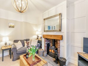 Una sala de estar con chimenea, un sofá, una mesa de centro con una botella y flores, y un televisor sobre un mueble.