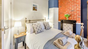 A neatly arranged bedroom with a bed, bedside table, lamp, and a fireplace with a brick wall. - Pennypot Cottage - UK41787 (Kettlewell)