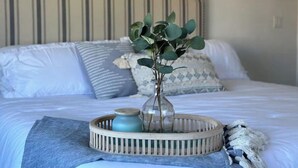 A neatly made bed with a striped headboard, a vase with green leaves, and a blue jar on a woven tray. - Modern Beach Cottage - Just Steps to the Ocean and Down Town Cocoa Beach (Cocoa Beach)