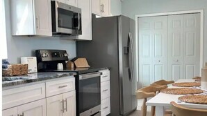 A modern kitchen with white cabinets, stainless steel appliances, and a dining area with wooden chairs. - Modern Beach Cottage - Just Steps to the Ocean and Down Town Cocoa Beach (Cocoa Beach)