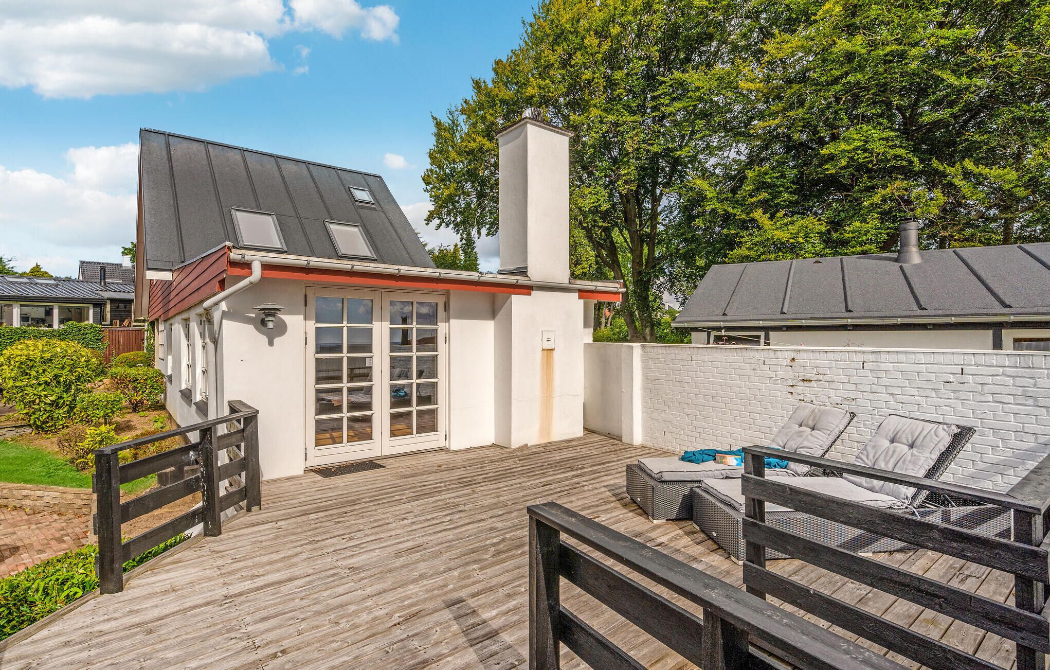 Een huis met een houten terras, een witte gevel en een schoorsteen.