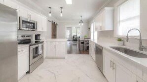 A modern kitchen with white cabinetry, stainless steel appliances, and a marble floor.