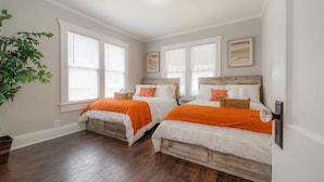 A bedroom with two beds, large windows, and a ceiling light.
