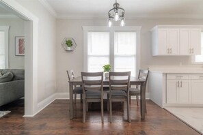Un coin repas avec une table et des chaises, un lustre et une cuisine dotée de meubles blancs.