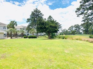 A residential area with a grassy lawn, trees, and a building with a fence. - Peaceful condo in the center of Myrtle Beach (Myrtle Beach)