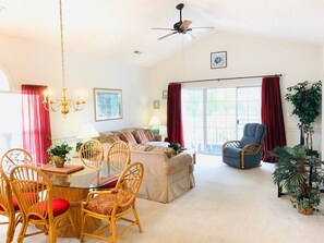 A spacious living room with a glass dining table, comfortable seating, a ceiling fan, and large windows with red curtains. - Peaceful condo in the center of Myrtle Beach (Myrtle Beach)