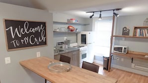 A modern kitchen with a wooden dining table, built-in appliances, and a 'Welcome to MY Crib' sign. - Cute & Cozy North End Studio (Detroit)