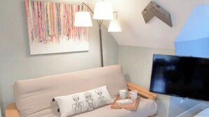 A modern living room with a beige sofa, a flat-screen TV, and a wooden side table with a tray of items. - Cute & Cozy North End Studio (Detroit)
