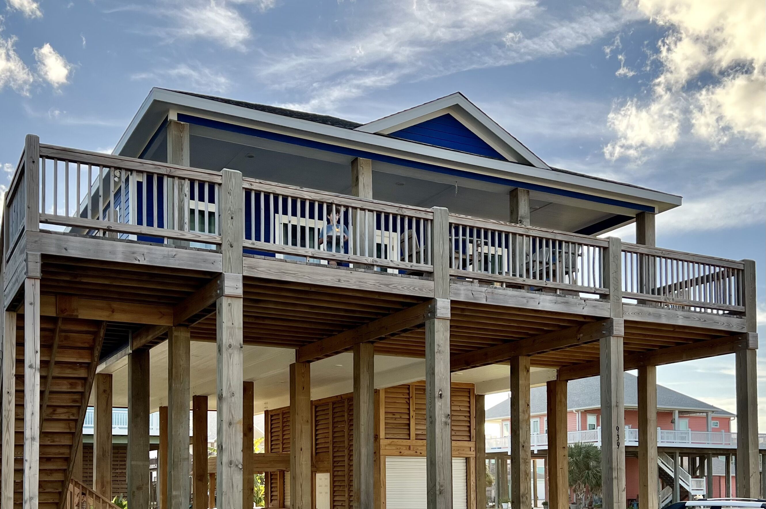 A two-story wooden structure with a balcony, supported by wooden beams, under a clear sky.