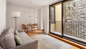 Una sala de estar moderna con un sofá, una mesa de comedor con sillas, una lámpara y un ventanal con vistas a un muro de piedra.