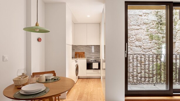 Una cocina moderna con armarios blancos, un salpicadero de mármol y un comedor con mesa y sillas de madera.