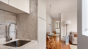 A modern kitchen with a marble backsplash and stainless steel sink, leading to a dining area with wooden flooring and a round table. - JOIVY Stunning 1-bed flat with balcony (Porto)