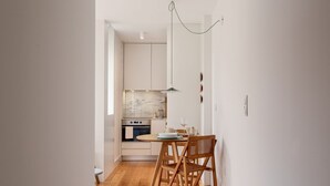 A modern kitchen with white cabinets, a marble backsplash, and a dining area with wooden chairs and a round table. - JOIVY Stunning 1-bed flat with balcony (Porto)