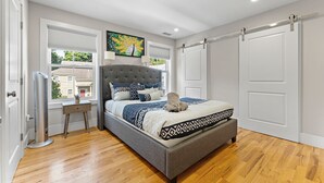 Een slaapkamer met een groot bed, een nachtkastje, een elektrische kachel en een raam met zonwering.