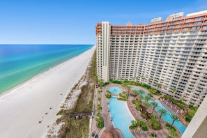 Um hotel alto com vista para a praia, piscina e um jardim bem cuidado.