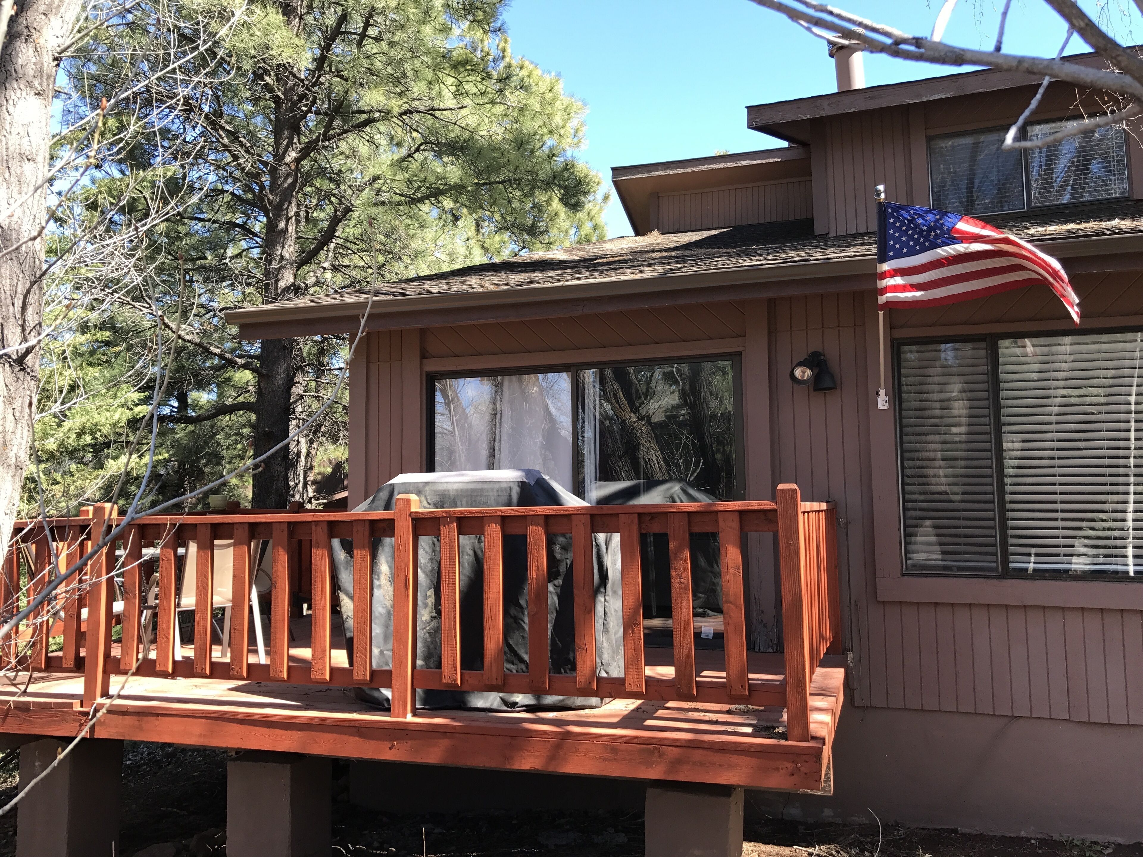 Une terrasse en bois avec un barbecue, un drapeau et un bâtiment doté de fenêtres.