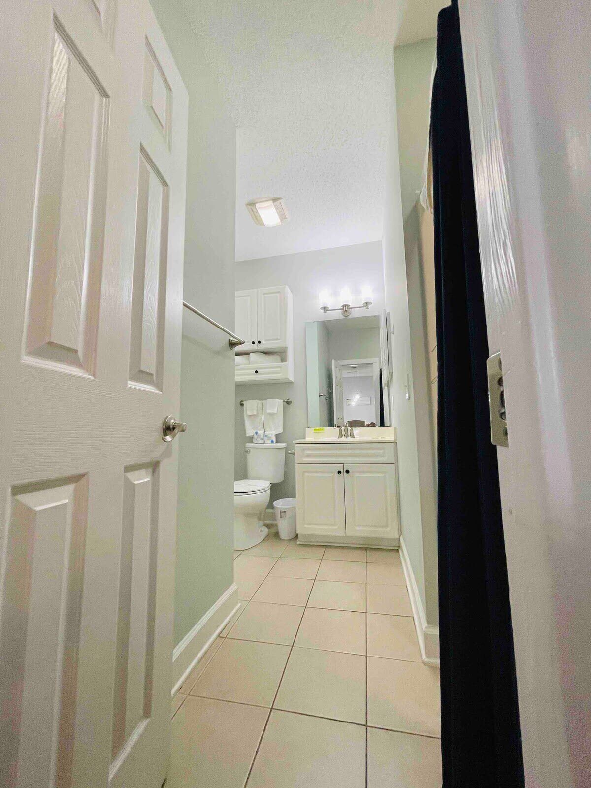 A narrow hallway leading to a bathroom with a toilet, sink, and mirror.