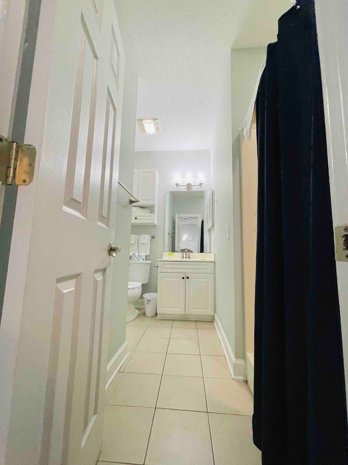 Un couloir étroit mène à une salle de bain équipée de toilettes, d’un lavabo et d’un miroir.
