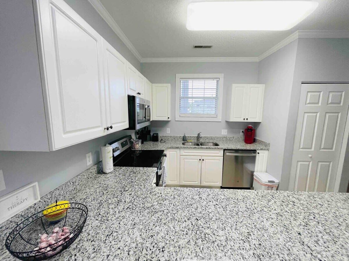 A kitchen with white cabinets, a granite countertop, a microwave, a sink, and a window with blinds.