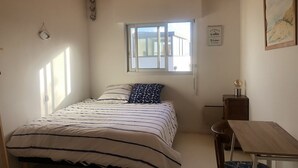 Un dormitorio con una cama, un escritorio, una silla, una ventana y una lámpara fijada a la pared.