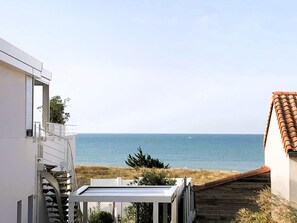 A coastal property with a view of the sea, a wooden deck, and a white building with a balcony.