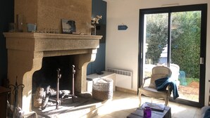 Una habitación con chimenea de piedra, una silla, una mesa y vistas a través de un ventanal.