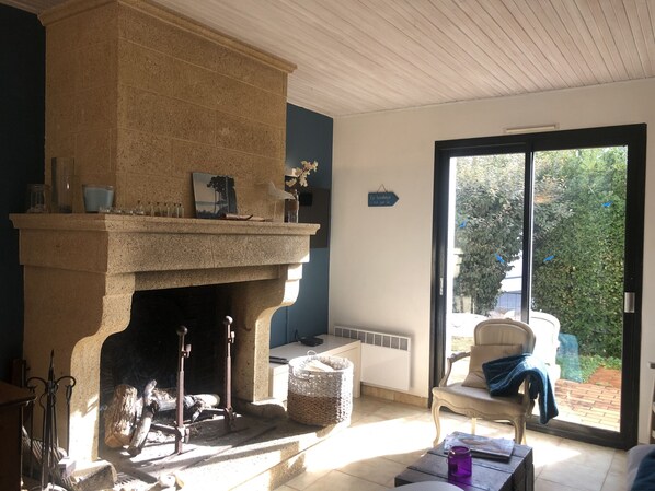 Een kamer met een stenen openhaard, een stoel, een tafel en een uitzicht door een glazen deur.
